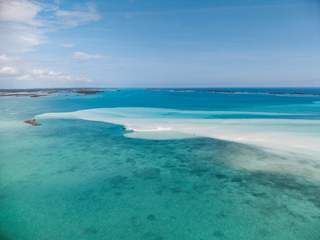 Aerial view of the Man O War Cay Sandbar surrounded by turquoise tropical waters and distant islands under a clear blue sky in Rolletown Exuma The Bahamas. Aerial view of the Man O War Cay Sandbar surrounded by turquoise tropical waters and distant islands under a clear blue sky in Rolletown Exuma The Bahamas.