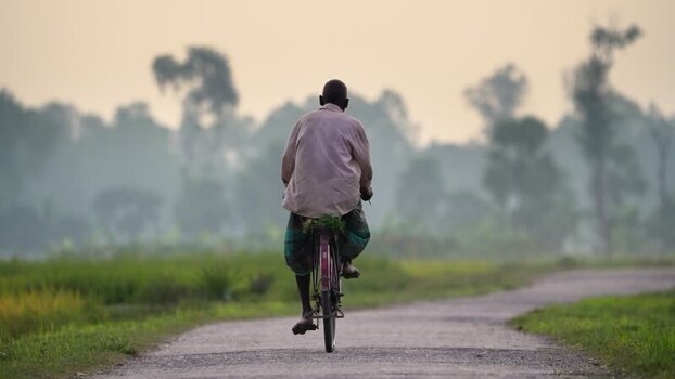 View of a man riding a bicycle on a rural road in Bangladesh.