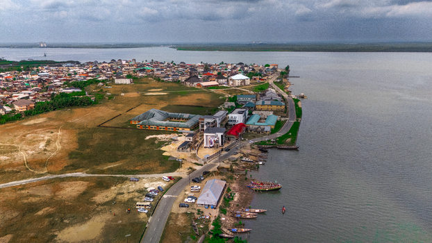 Aerial view of the coastal settlement along the riverbank featuring residential buildings a road and small boats moored at the shore in Minima Rivers Nigeria.