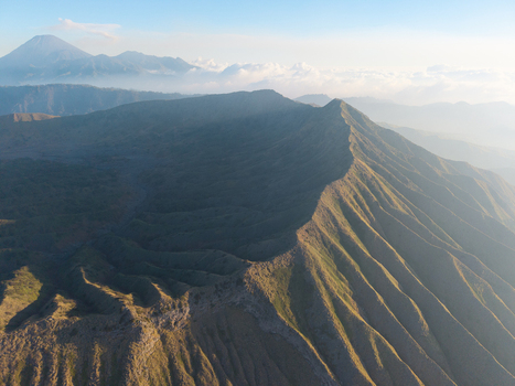 Aerial view of Mount Bromo featuring rugged volcanic ridges deep valleys and distant peaks under a soft morning light in Tosari East Java Indonesia.