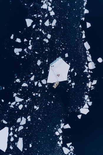 Aerial view of a boat moored to an ice floe with people surrounded by scattered ice fragments in deep blue arctic waters Tasiilaq Sermersooq Municipality Greenland. Aerial view of a boat moored to an ice floe with people surrounded by scattered ice fragments in deep blue arctic waters Tasiilaq Sermersooq Municipality Greenland.