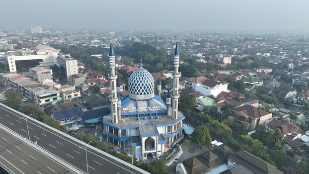 Aerial view of Masjid Jami Al Azhar Jakapermai with its distinctive blue dome and minarets surrounded by residential rooftops and a nearby highway in Bekasi Barat West Java Indonesia. Aerial view of Masjid Jami Al Azhar Jakapermai with its distinctive blue dome and minarets surrounded by residential rooftops and a nearby highway in Bekasi Barat West Java Indonesia.