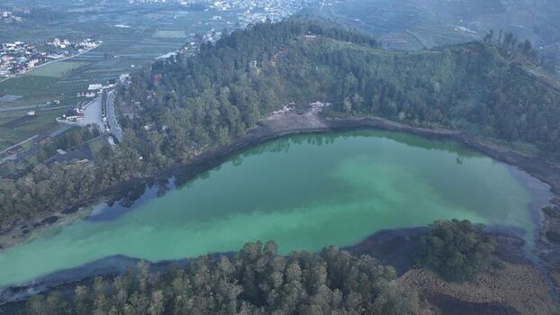 Aerial view of Dieng volcanic lake with turquoise water surrounded by lush green hills and forest in Kejajar Central Java Indonesia. Aerial view of Dieng volcanic lake with turquoise water surrounded by lush green hills and forest in Kejajar Central Java Indonesia.