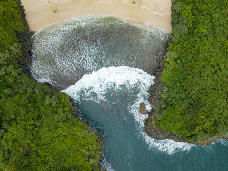 Aerial view of turquoise waves crashing against the rocky cliffs surrounding Sedahan Beach s golden sands Gunungkidul Regency Special Region of Yogyakarta Indonesia. Aerial view of turquoise waves crashing against the rocky cliffs surrounding Sedahan Beach s golden sands Gunungkidul Regency Special Region of Yogyakarta Indonesia.