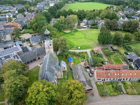Aerial view of Nicolaaskerk surrounded by lush green trees historic buildings and residential houses in Dwingeloo Drenthe Netherlands. Aerial view of Nicolaaskerk surrounded by lush green trees historic buildings and residential houses in Dwingeloo Drenthe Netherlands.