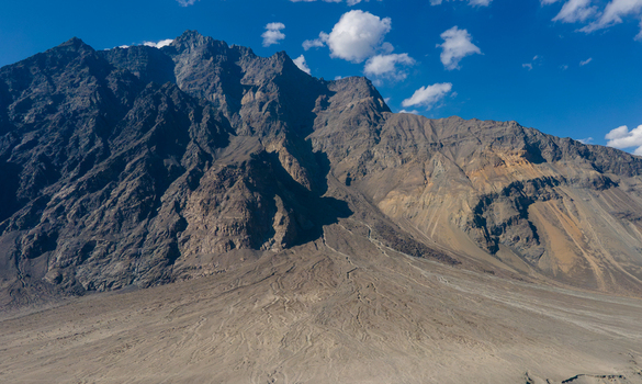 Aerial view of the Shigar River valley featuring rugged mountain slopes a vast dry riverbed and clear blue sky in Skardu Gilgit Pakistan.