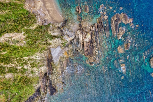 Aerial view of Silence Beach Viewpoint with jagged rock formations and turquoise water along the green coastline in Cudillero Asturias Spain.
