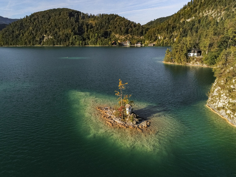 Aerial view of Ochsenkreuz on a small island in the middle of a clear lake surrounded by forested mountains in Salzburg Umgebung Salzburg Austria.