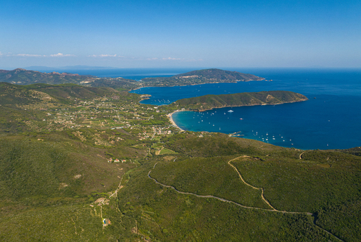 Aerial view of Lacona Beach on the island of Elba featuring turquoise waters sandy shores and lush green hills under a clear blue sky in Lacona Tuscany Italy.