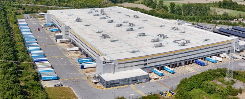 Torrazza Piemonte Italy 03 May 2026 Aerial view of the Amazon TRN1 fulfillment center with blue delivery trucks parked at loading docks surrounded by lush green trees and fields. Torrazza Piemonte Italy 03 May 2026 Aerial view of the Amazon TRN1 fulfillment center with blue delivery trucks parked at loading docks surrounded by lush green trees and fields.