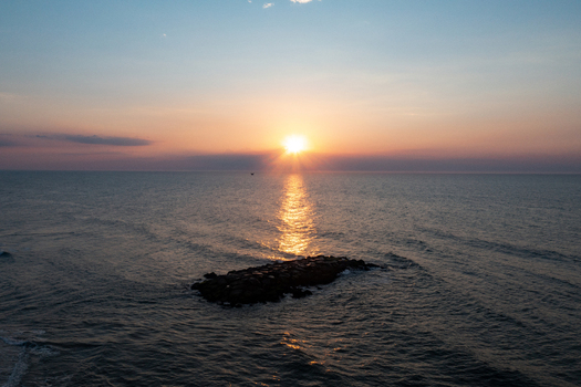 Aerial view of Asbury Park Beach at sunrise with golden light reflecting on the ocean waves and a stone jetty in Asbury Park New Jersey United States.
