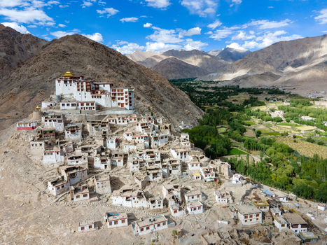Aerial view of Thiksey Monastery perched on a hillside with traditional white buildings surrounding arid mountain landscape and lush green valley below in Leh Ladakh India. Aerial view of Thiksey Monastery perched on a hillside with traditional white buildings surrounding arid mountain landscape and lush green valley below in Leh Ladakh India.