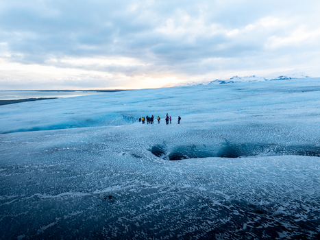 Aerial view of Breidamerkurjokull glacier with a group of hikers walking on the blue ice near a crevasse under a cloudy sky in Sveitarfelagid Hornafjordur Iceland. Aerial view of Breidamerkurjokull glacier with a group of hikers walking on the blue ice near a crevasse under a cloudy sky in Sveitarfelagid Hornafjordur Iceland.