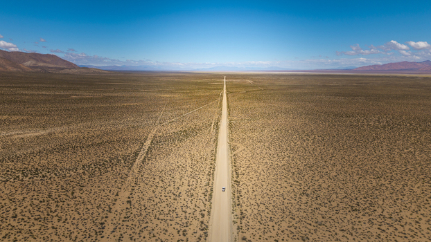 Aerial view of a long straight road cutting through the vast arid desert landscape under a clear blue sky with a single vehicle driving along the path Argentina. Aerial view of a long straight road cutting through the vast arid desert landscape under a clear blue sky with a single vehicle driving along the path Argentina.