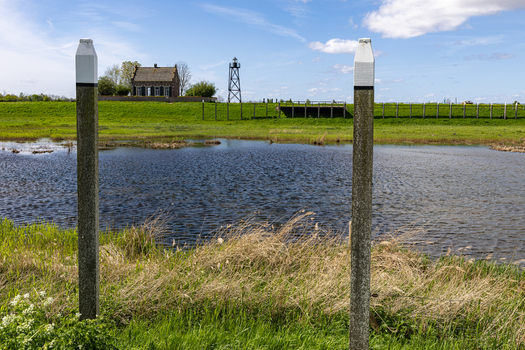 View of the historic Middelbuurt house and lighthouse frame across a marshy landscape with wooden poles in Schokland Flevoland Netherlands.