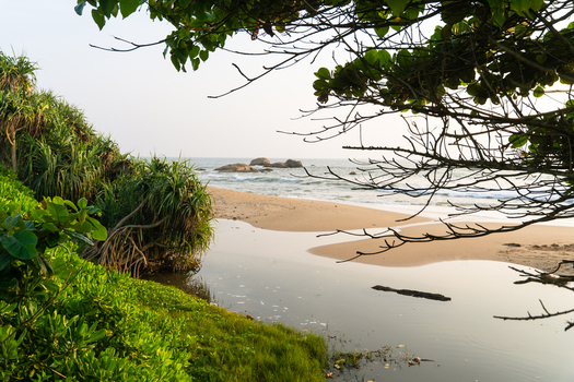 View of a tropical beach where a calm lagoon meets the ocean framed by lush green vegetation and coastal trees under a soft sky Galle Southern Province Sri Lanka.