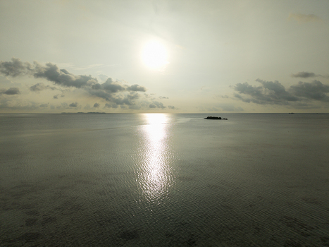 Aerial view of the sun reflecting off the calm sea waters with a distant island silhouette against the horizon at Bobby Beach Karimunjawa Central Java Indonesia.