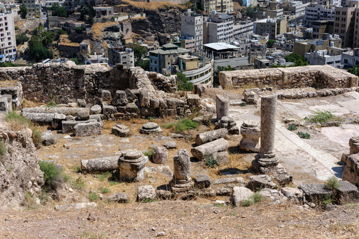 View of the ancient stone ruins and weathered columns of the Amman Citadel overlooking the dense urban cityscape of Amman Amman Governorate Jordan.