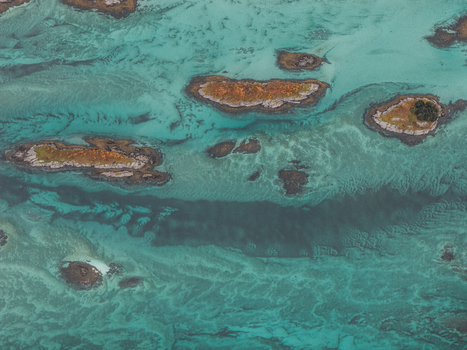 Aerial view of small rocky islands surrounded by turquoise shallow waters and sandy seabed patterns in Senja Troms Norway.