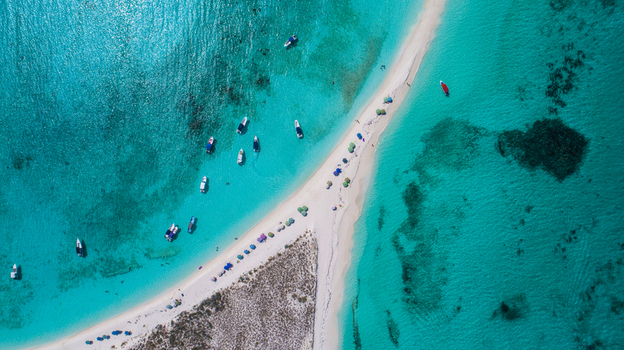 Aerial view of the Los Roques archipelago featuring a white sandbar in turquoise waters with anchored motorboats and people on the beach Los Roques Dependencias Federale Venezuela. Aerial view of the Los Roques archipelago featuring a white sandbar in turquoise waters with anchored motorboats and people on the beach Los Roques Dependencias Federale Venezuela.