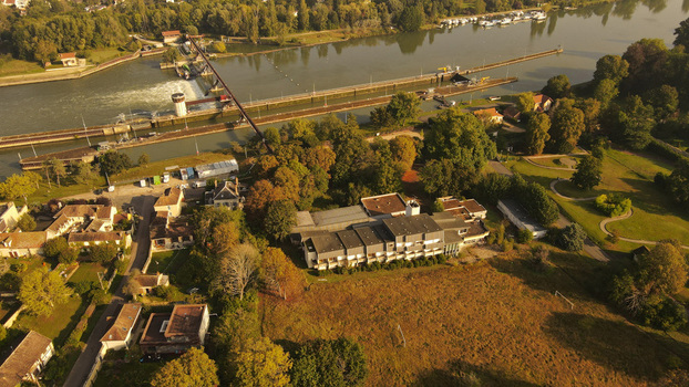 Aerial view of the Seine river lock system and surrounding buildings in the village of Chartrettes featuring lush trees and golden hour light in Chartrettes Ile de France France. Aerial view of the Seine river lock system and surrounding buildings in the village of Chartrettes featuring lush trees and golden hour light in Chartrettes Ile de France France.