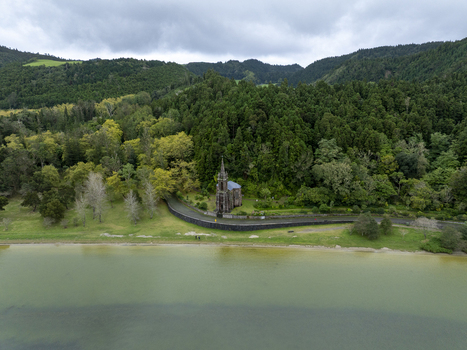 Aerial view of Ermida de Nossa Senhora das Vitorias situated on the shore of Lagoa das Furnas surrounded by lush green forest and hills in Furnas Acores Portugal. Aerial view of Ermida de Nossa Senhora das Vitorias situated on the shore of Lagoa das Furnas surrounded by lush green forest and hills in Furnas Acores Portugal.