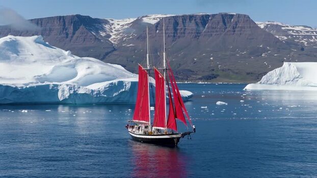 Aerial view of a sailboat with red sails in a glacial bay Greenland. Aerial view of a sailboat with red sails in a glacial bay Greenland.