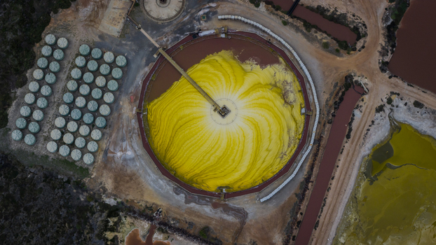 Aerial view of a large circular industrial mineral processing site with a vibrant yellow pile of salt surrounding storage tanks and textured ponds in Kalbarri Western Australia Australia. Aerial view of a large circular industrial mineral processing site with a vibrant yellow pile of salt surrounding storage tanks and textured ponds in Kalbarri Western Australia Australia.