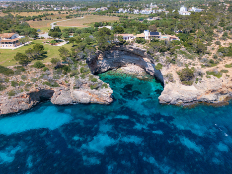 Aerial view of Cala Llombards featuring turquoise waters rugged rocky cliffs and coastal villas nestled among green trees in Cala Llombards Illes Balears Spain. Aerial view of Cala Llombards featuring turquoise waters rugged rocky cliffs and coastal villas nestled among green trees in Cala Llombards Illes Balears Spain.