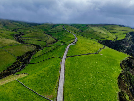 Aerial view of a winding road cuts through verdant hills a vibrant green tapestry under a cloudy sky Estrada do Farol Flores A&ccedil;ores Portugal.
