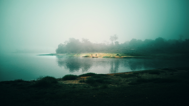 Aerial view of the misty Owala Reservoir with people standing on the shore surrounded by lush vegetation in Osogbo Osun Nigeria. Aerial view of the misty Owala Reservoir with people standing on the shore surrounded by lush vegetation in Osogbo Osun Nigeria.