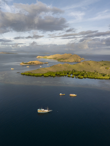 Aerial view of Komodo Island with lush green hills calm blue waters and traditional wooden boats sailing in the bay in Komodo East Nusa Tenggara Indonesia.