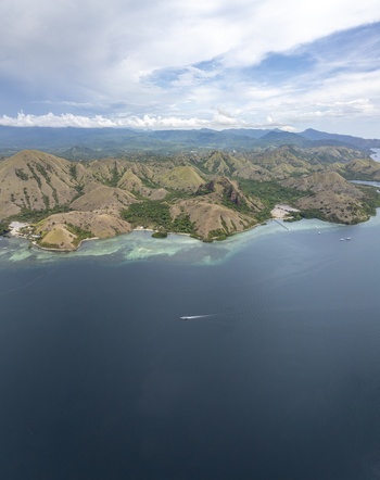 Aerial view of Komodo Island with its distinctive hilly landscape turquoise waters and a small boat cruising in the sea in Komodo East Nusa Tenggara Indonesia. Aerial view of Komodo Island with its distinctive hilly landscape turquoise waters and a small boat cruising in the sea in Komodo East Nusa Tenggara Indonesia.