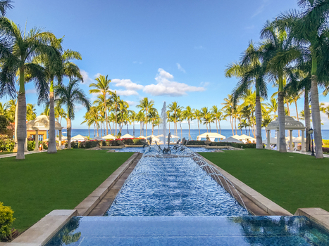 View of a decorative fountain in a lush resort garden with palm trees and manicured lawns overlooking the ocean in Maui County Hawaii United States.