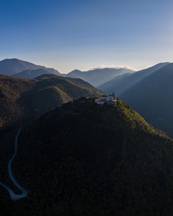 Aerial view of Santuario del Santissimo Salvatore on a mountain peak with winding roads and sunbeams over the hills in Montella Campania Italy. Aerial view of Santuario del Santissimo Salvatore on a mountain peak with winding roads and sunbeams over the hills in Montella Campania Italy.