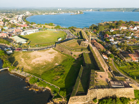 Aerial view of the historic Galle Fort and the international cricket stadium along the scenic coastline under a clear blue sky in Galle Southern Province Sri Lanka.