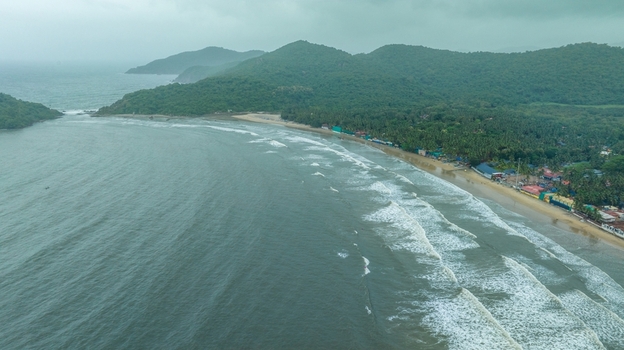 Aerial view of Palolem Beach with lush green hills palm trees and waves crashing on the sandy shore in Canacona Goa India.
