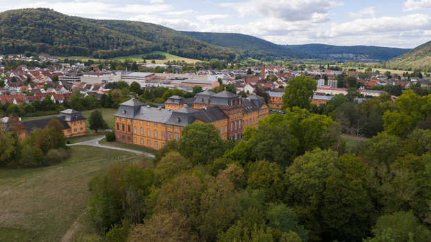 Aerial view of Chateauform Schloss Lowenstein surrounded by lush green trees rolling hills and the town of Kleinheubach in the background under a cloudy sky Kleinheubach Bayern Germany. Aerial view of Chateauform Schloss Lowenstein surrounded by lush green trees rolling hills and the town of Kleinheubach in the background under a cloudy sky Kleinheubach Bayern Germany.