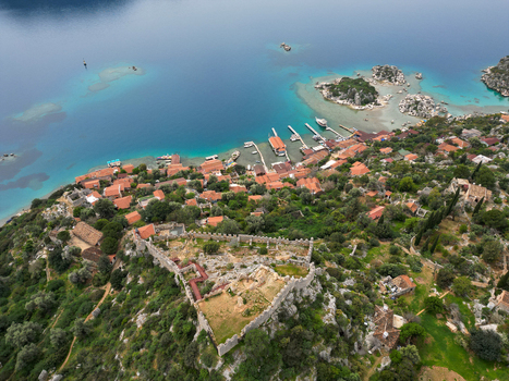 Aerial view of the historic fortress of Simena overlooking the turquoise Mediterranean Sea with red tiled rooftops and boats docked along the coastline in Demre Antalya Turkiye. Aerial view of the historic fortress of Simena overlooking the turquoise Mediterranean Sea with red tiled rooftops and boats docked along the coastline in Demre Antalya Turkiye.
