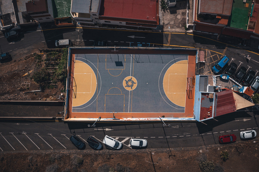 Aerial view of a colorful basketball court with a central sun logo surrounded by urban buildings and parked cars in Bocacangrejo Canarias Spain. Aerial view of a colorful basketball court with a central sun logo surrounded by urban buildings and parked cars in Bocacangrejo Canarias Spain.