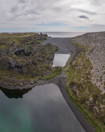 Aerial view of Djupalonssandur beach featuring black volcanic sand rugged rock formations and calm pools of water along the coastline of Iceland. Aerial view of Djupalonssandur beach featuring black volcanic sand rugged rock formations and calm pools of water along the coastline of Iceland.