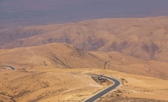 Aerial view of Mount Nebo featuring a winding road cutting through the arid desert landscape with rolling hills in Faisaliah Sub District Madaba Governorate Jordan. Aerial view of Mount Nebo featuring a winding road cutting through the arid desert landscape with rolling hills in Faisaliah Sub District Madaba Governorate Jordan.