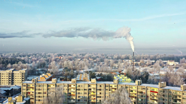 Aerial view of a residential area with apartment buildings and a smoking chimney amidst snow covered trees in winter in Latvia. Aerial view of a residential area with apartment buildings and a smoking chimney amidst snow covered trees in winter in Latvia.