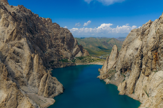 Aerial view of the turquoise waters of Kol Suu lake surrounded by steep jagged rocky cliffs under a blue sky in At Bashi District Naryn Region Kyrgyzstan.