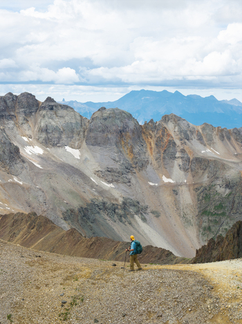 Aerial view of a hiker with a backpack and trekking pole on a rocky ridge overlooking the peaks of Mount Sneffels in the San Juan Mountain Range near Ouray Colorado United States. Aerial view of a hiker with a backpack and trekking pole on a rocky ridge overlooking the peaks of Mount Sneffels in the San Juan Mountain Range near Ouray Colorado United States.