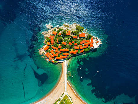 Aerial view of the historic islet of Sveti Stefan with its terracotta roofed buildings and sandy isthmus surrounded by the turquoise Adriatic Sea in Sveti Stefan Budva Municipality Montenegro.