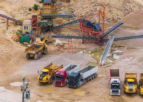 Aerial view of a gravel pit featuring heavy machinery conveyor belts and several dump trucks parked on a sandy site in Tczew Pomeranian Voivodeshi Poland. Aerial view of a gravel pit featuring heavy machinery conveyor belts and several dump trucks parked on a sandy site in Tczew Pomeranian Voivodeshi Poland.