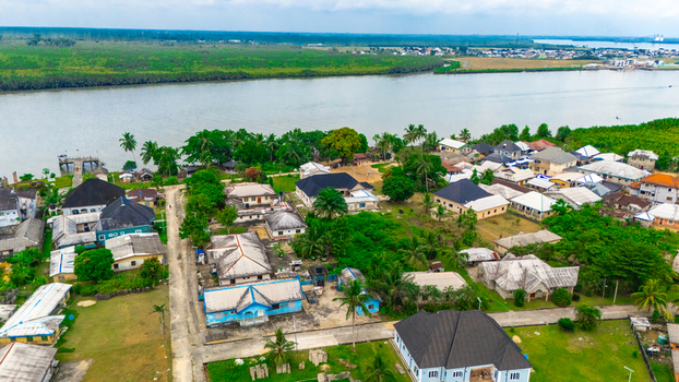 Aerial view of a riverside settlement featuring residential houses lush tropical vegetation and a small jetty extending into the river in Minima Rivers Nigeria.