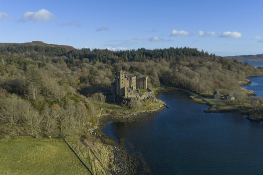Aerial view of Dunvegan Castle and Gardens a historic stone fortress on a rocky promontory surrounded by dense woodland and a calm loch Isle of Skye Scotland United Kingdom. Aerial view of Dunvegan Castle and Gardens a historic stone fortress on a rocky promontory surrounded by dense woodland and a calm loch Isle of Skye Scotland United Kingdom.