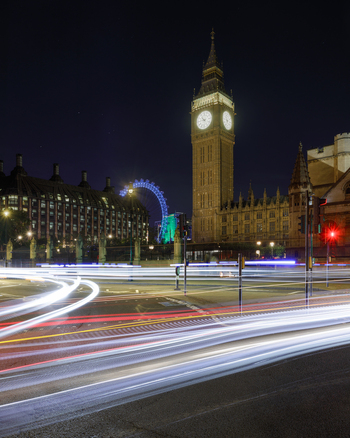 View of Big Ben illuminated at night with light trails from passing traffic on the streets of London England United Kingdom.